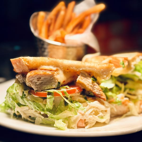 Chicken sandwich with melted cheese, lettuce, and tomatoes, served with a side of fries.