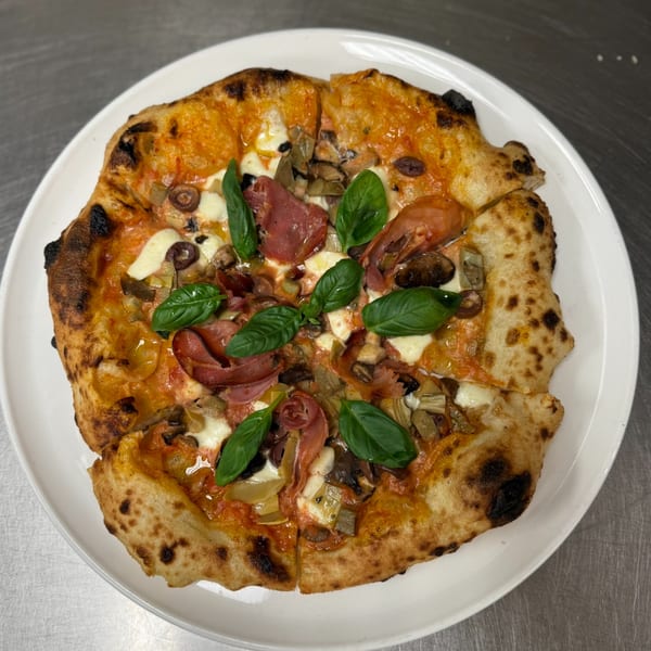 Mikas Neapolitan pizza with prosciutto, mushrooms, olives, and basil on a white plate.