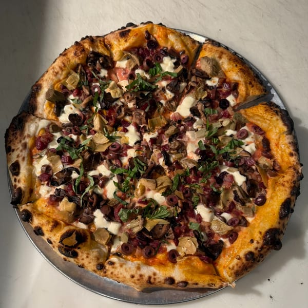 Mikas Neapolitan Pizza with mushrooms, olives, artichokes, and fresh basil on a metal tray.