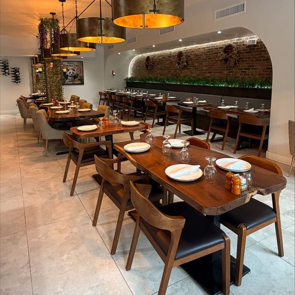 Warmly lit Italian restaurant dining room with neatly set wooden tables, leather chairs, pendant lights, and exposed brick accents.