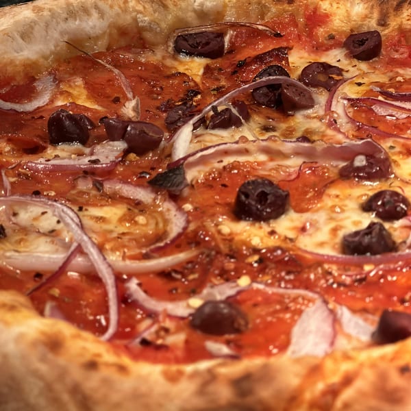 Close-up of a Mikas Neapolitan pizza with red sauce, melted cheese, black olives, and red onions.