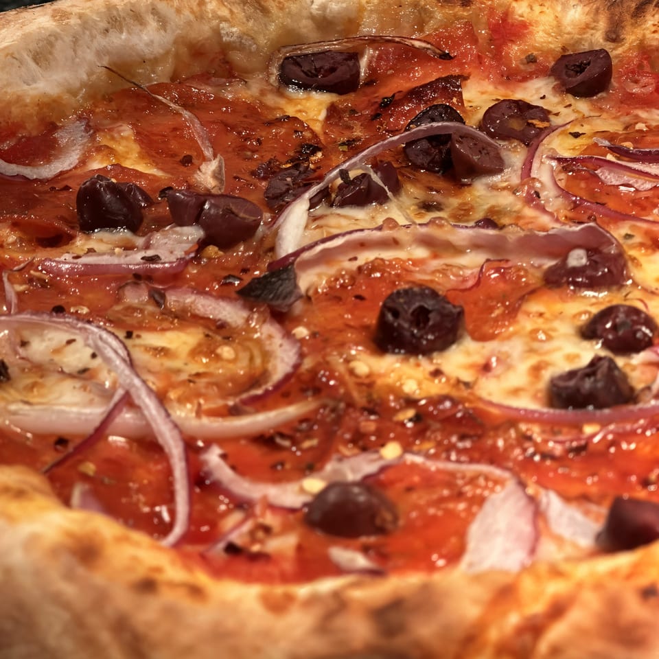 Close-up of a Mikas Neapolitan pizza with red sauce, melted cheese, red onions, and black olives.