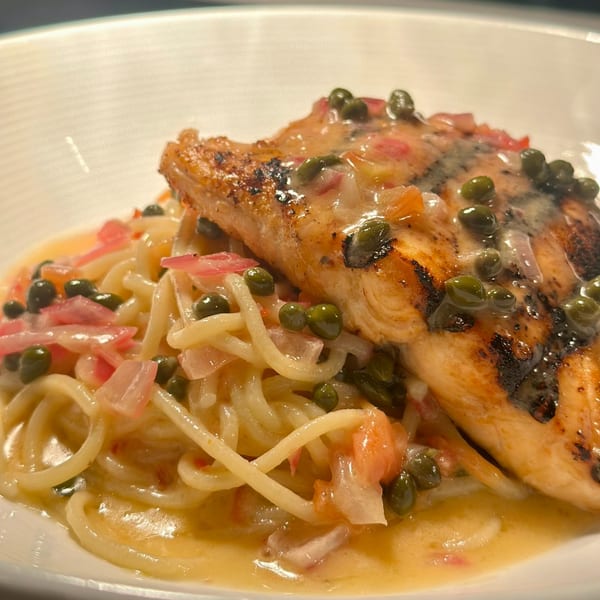 Grilled salmon with capers and sauce, served over spaghetti with diced red onions.