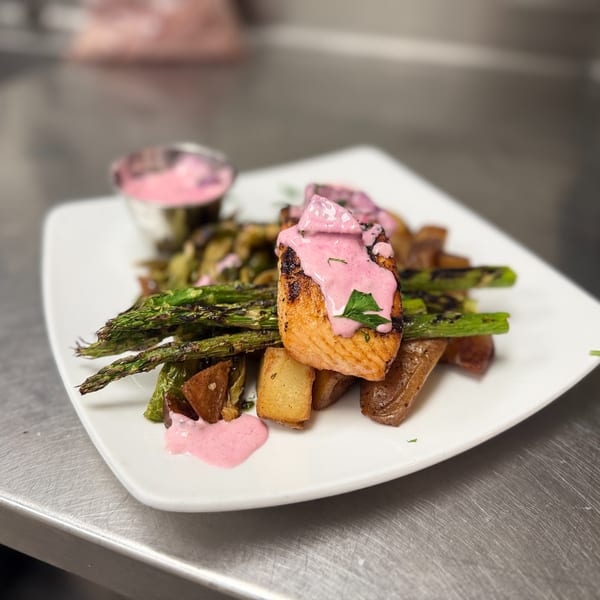 Grilled salmon with pink sauce, roasted potatoes, and asparagus on a white plate.