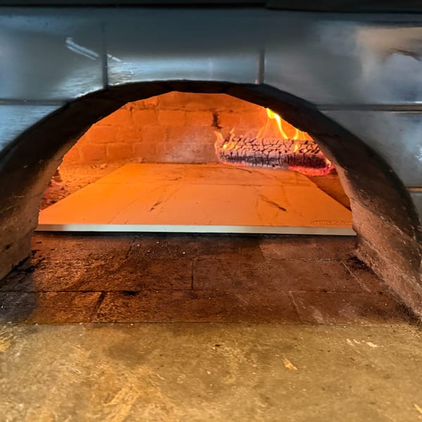 A wood-fired pizza oven with glowing embers and flames, ready for baking.