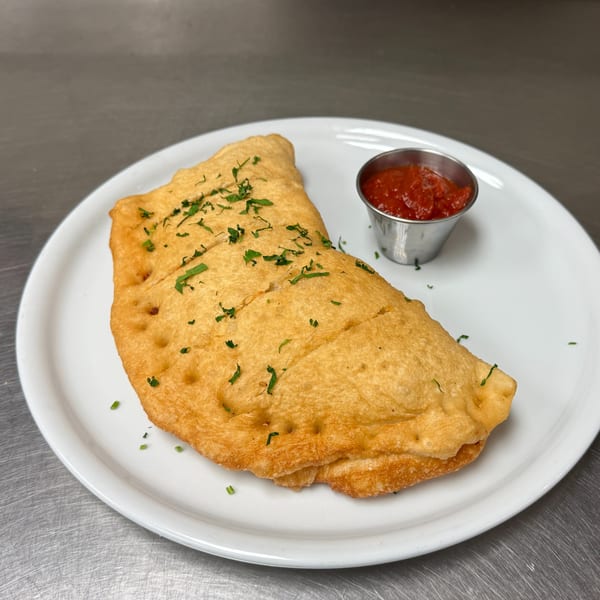 Golden-brown Mikas Neapolitan Pizza calzone, sprinkled with herbs, served with a side of red sauce.